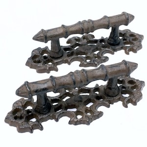 May include: Two antique-style cast iron door handles with intricate scrollwork and a decorative bar. The handles are a dark brown color.