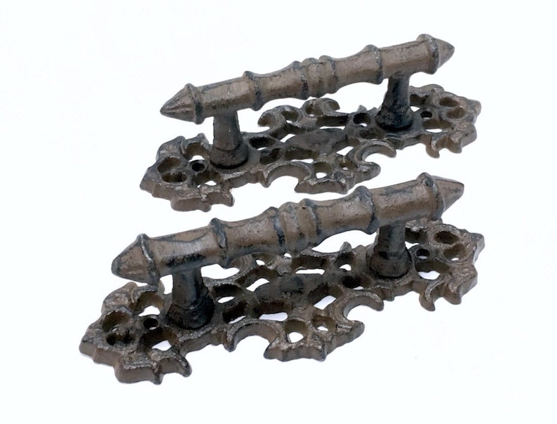 Puede incluir: Dos tiradores de puerta de hierro fundido de estilo antiguo con intrincados adornos y una barra decorativa. Los tiradores son de color marr&oacute;n oscuro.