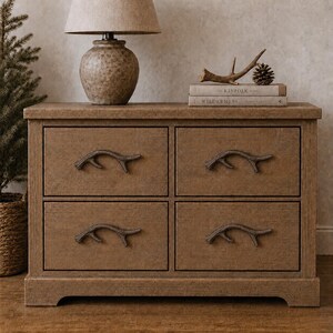 Puede incluir: Una cómoda rectangular de madera con cuatro cajones, cada uno con un tirador en forma de cornamenta de color marrón oscuro. El mueble tiene un acabado texturizado en marrón medio y se asienta sobre una base plana con una lámpara y libros.