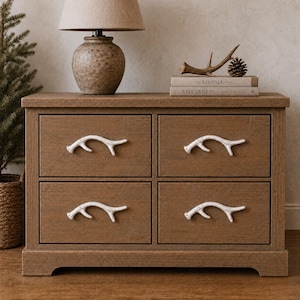 Op de afbeelding: Een bruine houten ladekast met vier lades en witte handgrepen in de vorm van een gewei. De kast heeft een rechthoekig frame met een plat bovenoppervlak en elke lade is voorzien van een decoratieve handgreep in de vorm van een hertengewei.