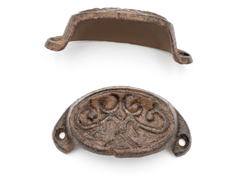 Peut inclure: Deux poign&eacute;es de tiroir en fonte de style antique, marron. L'une est vue de c&ocirc;t&eacute;, l'autre de face. La poign&eacute;e orient&eacute;e vers l'avant pr&eacute;sente un motif floral orn&eacute;. Chaque poign&eacute;e a deux trous de montage.