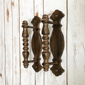 May include: Three cast iron door handles with a rustic brown finish. The handles have a decorative, ornate design with a rounded shape.
