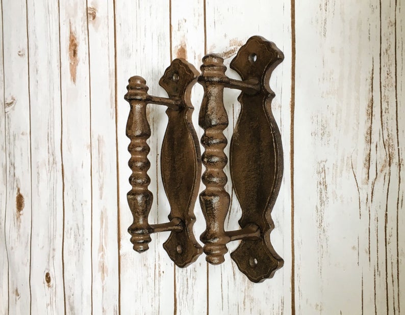 May include: Three cast iron door handles with a rustic brown finish. The handles have a decorative, ornate design with a rounded shape.
