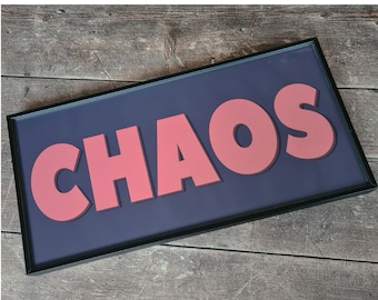 May include: A black framed sign with the word "CHAOS" in large, pink, 3D letters on a dark blue background.