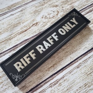 Pu&ograve; includere: Un cartello in legno nero con lettere argentate che recita "Riff Raff Only".