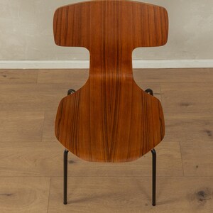 Puede incluir: Silla de estilo retro con un respaldo en forma de T. El asiento y el respaldo son de madera con una veta c&aacute;lida, sostenidos por finas patas de metal negro. El dise&ntilde;o es minimalista y funcional, adecuado para varios estilos de interior. Medidas en cent&iacute;metros.