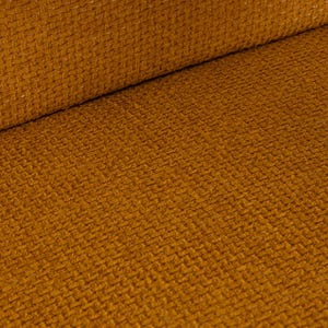 May include: Close-up of a textured fabric in a warm, golden-brown hue. The material has a woven appearance with a subtle diagonal pattern. The fabric is folded over, revealing a rolled edge.