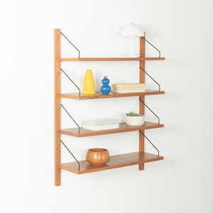 Peut inclure: Étagère murale de style moderne du milieu du siècle avec quatre étagères en bois. Les étagères sont soutenues par des supports en métal noir et un support vertical en bois. Articles décoratifs : lampe blanche, vases et petite plante.