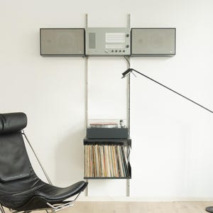May include: A black leather chair, a black floor lamp, and a wall-mounted stereo system with speakers and a turntable. The stereo system has a shelf with vinyl records. The room has a minimalist design.