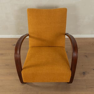 May include: An upholstered armchair with a mustard-yellow fabric seat and back. The chair has curved, dark wooden armrests. The design is mid-century modern, with a focus on comfort and style. The chair is set against a neutral background.