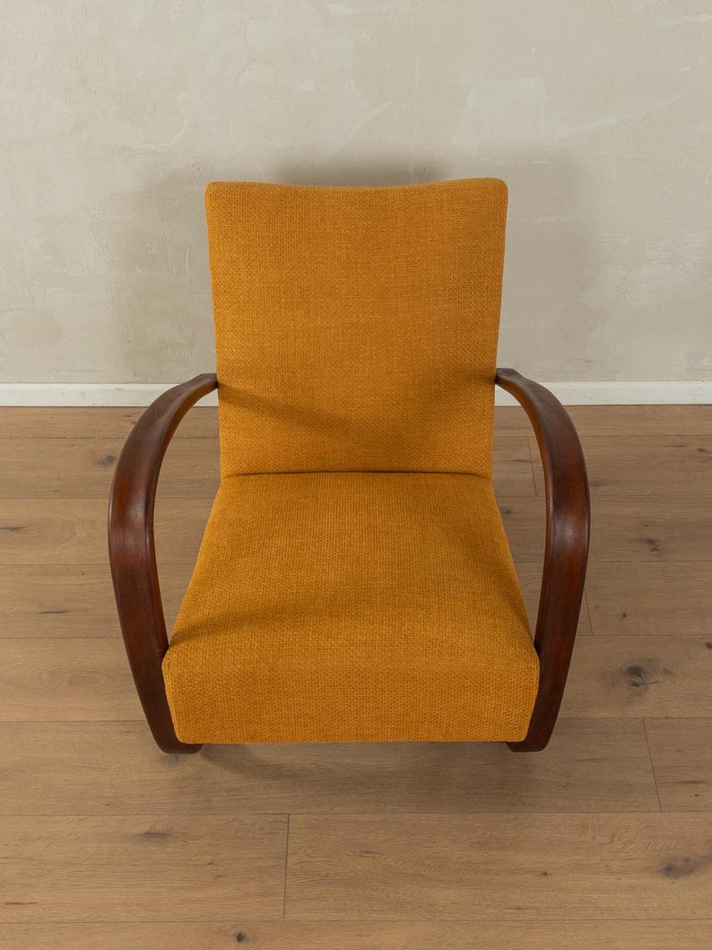 May include: An upholstered armchair with a mustard-yellow fabric seat and back. The chair has curved, dark wooden armrests. The design is mid-century modern, with a focus on comfort and style. The chair is set against a neutral background.