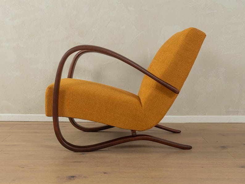 May include: An orange mid-century modern armchair with a curved wooden frame. The chair has a high back and a low seat, with a curved wooden armrest. The chair is upholstered in a textured orange fabric.