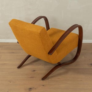 May include: An orange upholstered armchair with dark brown wooden frame and curved armrests. The chair has a low profile and a mid-century modern design, with a slightly reclined backrest and angled legs.
