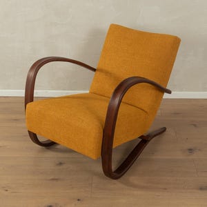 May include: Mustard yellow armchair with curved, dark wood arms and base. The chair has a textured fabric and a mid-century modern design. The wooden frame is a rich, dark brown color, and the chair is set on a wooden floor.