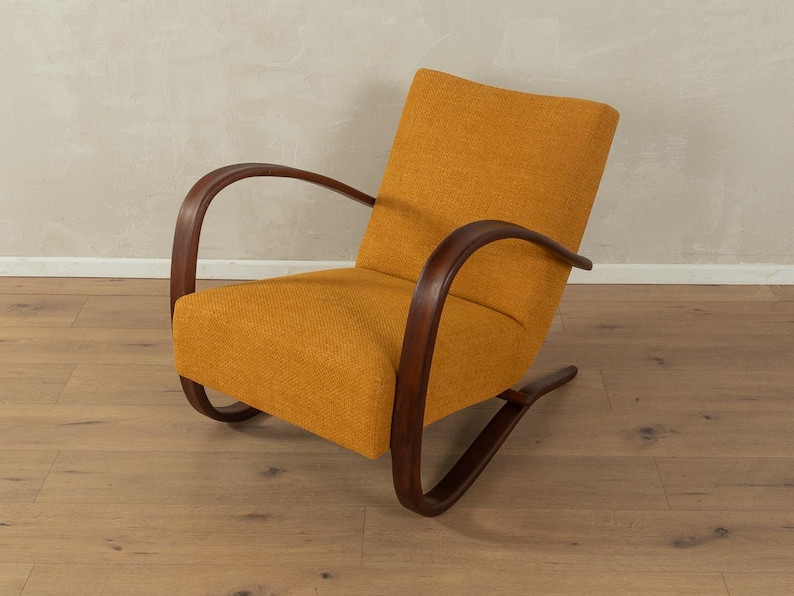 May include: Mustard yellow armchair with curved, dark wood arms and base. The chair has a textured fabric and a mid-century modern design. The wooden frame is a rich, dark brown color, and the chair is set on a wooden floor.