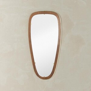 Puede incluir: Un espejo de pared de estilo moderno de mediados de siglo con una forma única de lágrima alargada. El espejo presenta un marco de madera de color nogal cálido con un fino borde metálico dorado. Pequeños detalles de color latón aseguran el marco.