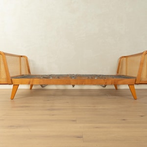 Può includere: Un divano letto moderno di metà secolo con struttura in legno chiaro e dettagli in canna intrecciata sui poggiatesta. Il letto presenta una base a molle e gambe angolate, offrendo un mix di stile e funzionalità. Il divano letto è lungo circa 190 cm.