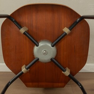 Puede incluir: Vista inferior de una silla moderna de mediados de siglo. La silla presenta un asiento de madera, patas de metal negro y un soporte central de metal. Las patas est&aacute;n unidas al asiento con conectores de goma o pl&aacute;stico de color beige.