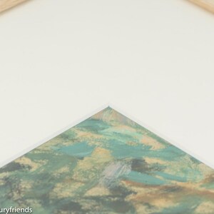 Puede incluir: Primer plano de una esquina de una obra de arte enmarcada. La obra presenta pinceladas abstractas en tonos verdes, azules y dorados.