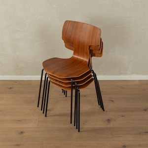 Puede incluir: Una pila de cuatro sillas de madera con respaldos curvos y patas de metal oscuro. Las sillas est&aacute;n hechas de madera de tonos c&aacute;lidos y tienen un dise&ntilde;o minimalista. Las sillas est&aacute;n apiladas una encima de otra.