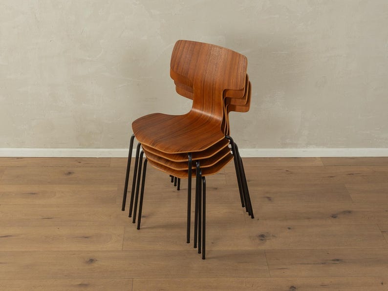 Puede incluir: Una pila de cuatro sillas de madera con respaldos curvos y patas de metal oscuro. Las sillas est&aacute;n hechas de madera de tonos c&aacute;lidos y tienen un dise&ntilde;o minimalista. Las sillas est&aacute;n apiladas una encima de otra.