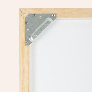 Puede incluir: Primer plano de una esquina de un marco de madera con una escuadra de esquina de metal. La escuadra est&aacute; asegurada con peque&ntilde;os tornillos.