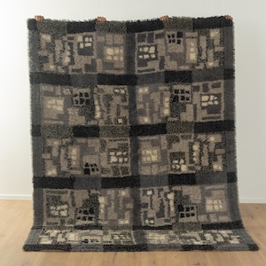 Peut inclure: Un tapis géométrique noir et gris à motifs avec une texture hirsute. Le tapis est de forme carrée et est fait de laine.