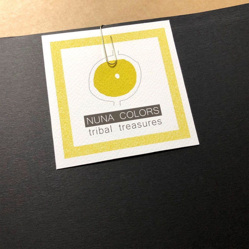 Peut inclure: Une &eacute;tiquette blanche avec une bordure jaune et un cercle jaune avec un cercle plus petit &agrave; l'int&eacute;rieur. Le texte "NUNA COLORS tribal treasures" est imprim&eacute; sur l'&eacute;tiquette.