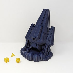 May include: A dark blue 3D printed spaceship with a cloud-like base. The spaceship is hovering above three yellow dice.