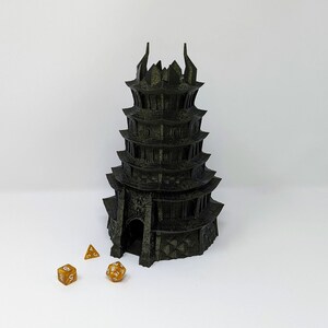 May include: A black 3D printed tower with a pointed roof and multiple levels. Three gold dice are in front of the tower.