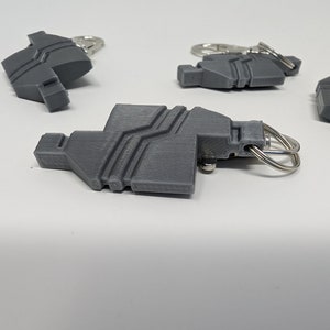 Puede incluir: Cuatro llaveros grises impresos en 3D con anillas de plata. Cada llavero tiene un diseño geométrico único.