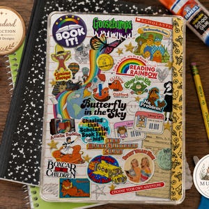 May include: A clear protective cover for a tablet or notebook, decorated with a collage of colorful stickers featuring nostalgic 1990s pop culture icons, book titles, and characters, including a butterfly, rainbows, and a yellow school bus.
