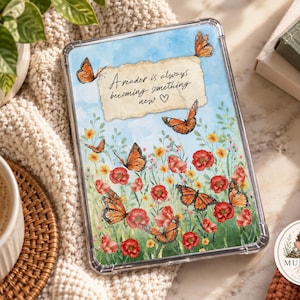Könnte beinhalten: Eine rechteckige Tablethülle mit einer Aquarellillustration von orangefarbenen Monarchfaltern und roten Mohnblumen vor einem hellblauen Himmel. Ein zentrales Stück Pergamentpapier zeigt den Text: A reader is always becoming something new.