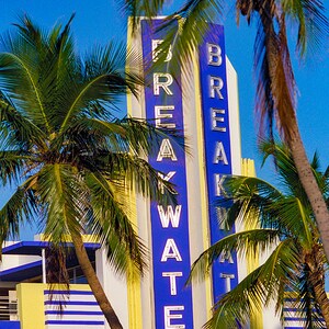 May include: A vintage art deco building with a blue and yellow striped facade. The building has a large sign that reads "BREAKWATER" in white letters. Two palm trees are in the foreground.