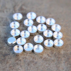 May include: A group of silver-colored metal cup-shaped settings for jewelry making.