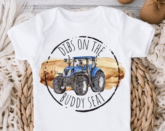 May include: White baby onesie with a blue tractor illustration and the text "Dibs on the Buddy Seat" in a black circle.