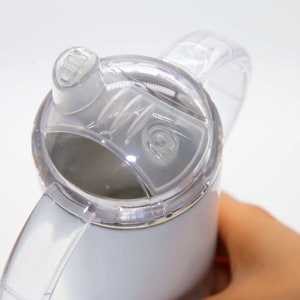 K&ouml;nnte beinhalten: Wei&szlig;e Reise-Thermoskanne aus Edelstahl mit einem durchsichtigen Deckel und einem durchsichtigen Griff. Der Deckel hat einen Klappverschluss zum Trinken.