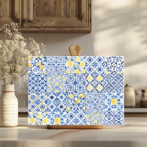 May include: A rectangular cutting board with a wooden handle. The board features a blue and white tile pattern with yellow lemons. The design is reminiscent of Mediterranean decor. The board is on a light-colored countertop.
