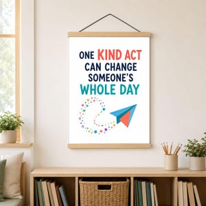 May include: A vertical wall hanging poster with a wooden frame and black string. The white print features the text ONE KIND ACT CAN CHANGE SOMEONE'S WHOLE DAY in red, blue, and teal, with a colorful paper airplane and small star icons.