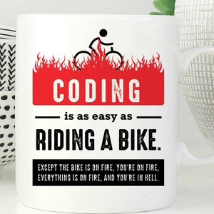 May include: A white ceramic mug featuring a graphic of a stick figure on a bicycle engulfed in red flames. The text reads: CODING is as easy as RIDING A BIKE. EXCEPT THE BIKE IS ON FIRE, YOU'RE ON FIRE, EVERYTHING IS ON FIRE, AND YOU'RE IN HELL.