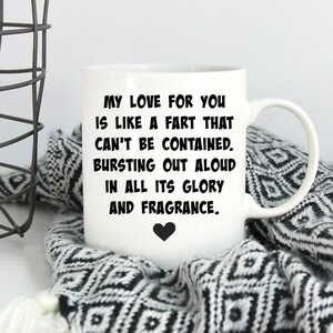 May include: A white ceramic mug featuring black text that reads: MY LOVE FOR YOU IS LIKE A FART THAT CAN'T BE CONTAINED. BURSTING OUT ALOUD IN ALL ITS GLORY AND FRAGRANCE. A small black heart icon is printed below the text on the front of the mug.