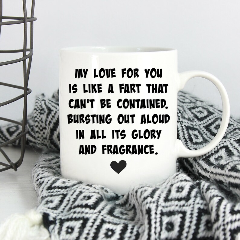 May include: A white ceramic mug featuring black text that reads: MY LOVE FOR YOU IS LIKE A FART THAT CAN'T BE CONTAINED. BURSTING OUT ALOUD IN ALL ITS GLORY AND FRAGRANCE. A small black heart icon is printed below the text on the front of the mug.