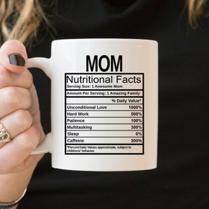 May include: A white ceramic mug featuring black text that reads MOM Nutritional Facts, listing ingredients like Unconditional Love 1000%, Hard Work 500%, Patience 100%, Multitasking 300%, Sleep 0%, and Caffeine 300%, with a disclaimer about children's behavior.