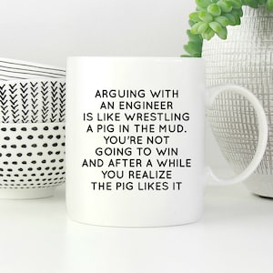 May include: A white ceramic mug featuring black text that reads: ARGUING WITH AN ENGINEER IS LIKE WRESTLING A PIG IN THE MUD. YOU'RE NOT GOING TO WIN AND AFTER A WHILE YOU REALIZE THE PIG LIKES IT. The mug has a standard handle and a smooth finish.
