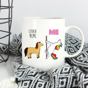 Peut inclure: Un mug en c&eacute;ramique blanche avec un motif comprenant le texte OTHER MOMS au-dessus d'un cheval beige et le texte ME en rose au-dessus d'une licorne blanche &agrave; la crini&egrave;re et &agrave; la queue arc-en-ciel effectuant une danse sur une barre verticale.