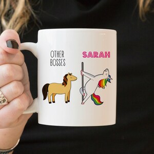 Puede incluir: Una taza de cer&aacute;mica blanca con un gr&aacute;fico que muestra el texto OTHER BOSSES sobre un caballo marr&oacute;n, y el nombre SARAH en letras rosas sobre un unicornio blanco con crin y cola de arco&iacute;ris bailando en una barra vertical.