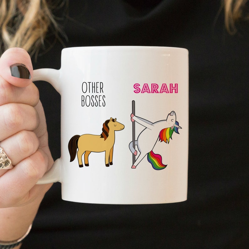 Puede incluir: Una taza de cer&aacute;mica blanca con un gr&aacute;fico que muestra el texto OTHER BOSSES sobre un caballo marr&oacute;n, y el nombre SARAH en letras rosas sobre un unicornio blanco con crin y cola de arco&iacute;ris bailando en una barra vertical.