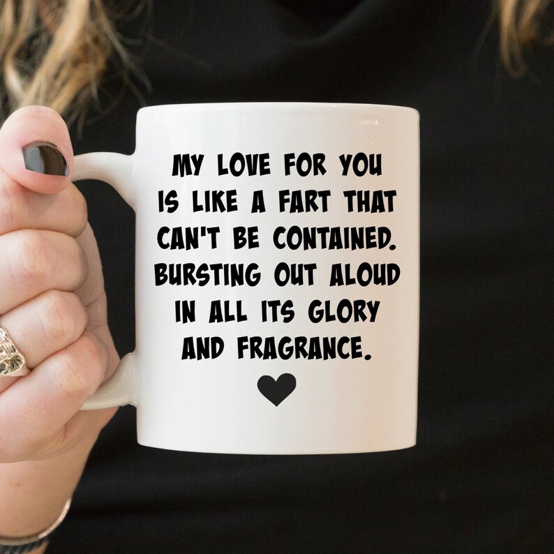 May include: A white ceramic mug featuring black text that reads: MY LOVE FOR YOU IS LIKE A FART THAT CAN'T BE CONTAINED. BURSTING OUT ALOUD IN ALL ITS GLORY AND FRAGRANCE. A small black heart icon is printed directly below the text on the mug.