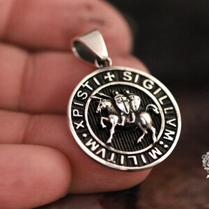 May include: Silver pendant with a black enamel design featuring a knight on horseback. The pendant is round and has the inscription "XPISTI SIGILLVM" around the edge.