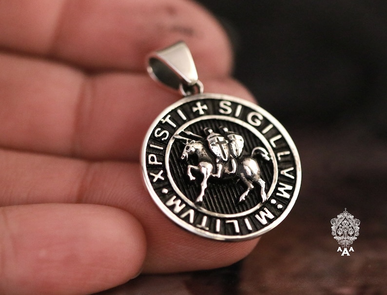 May include: Silver pendant with a black enamel design featuring a knight on horseback. The pendant is round and has the inscription "XPISTI SIGILLVM" around the edge.